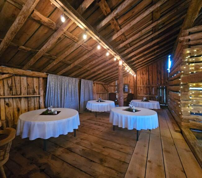 Indoor event space inside a historic rustic barn with wooden beams and round tables at Three Willows Ranch in Bayfield Colorado