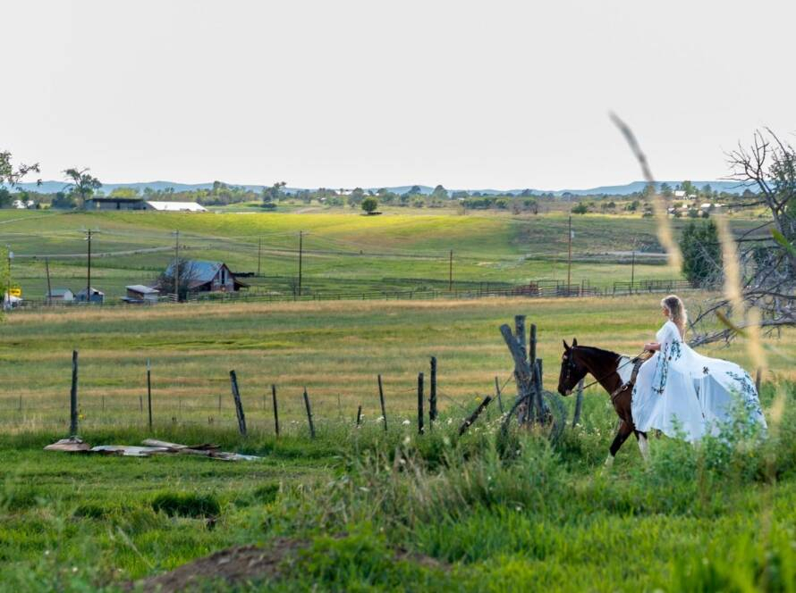 Bride riding horse across open ranch landscape at Three Willows Ranch wedding venue in Bayfield Colorado
