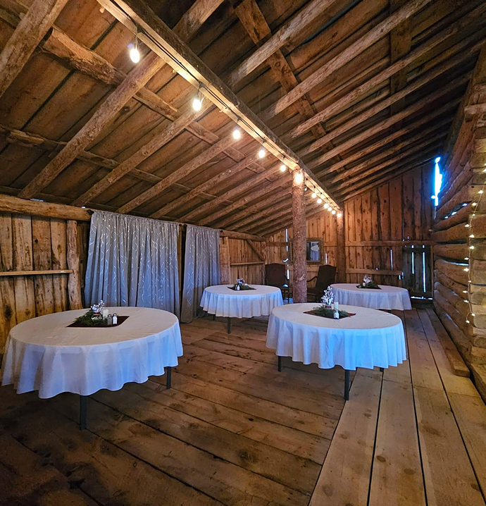 Cozy historic barn interior with string lights and round tables set for rustic wedding or private event reception.