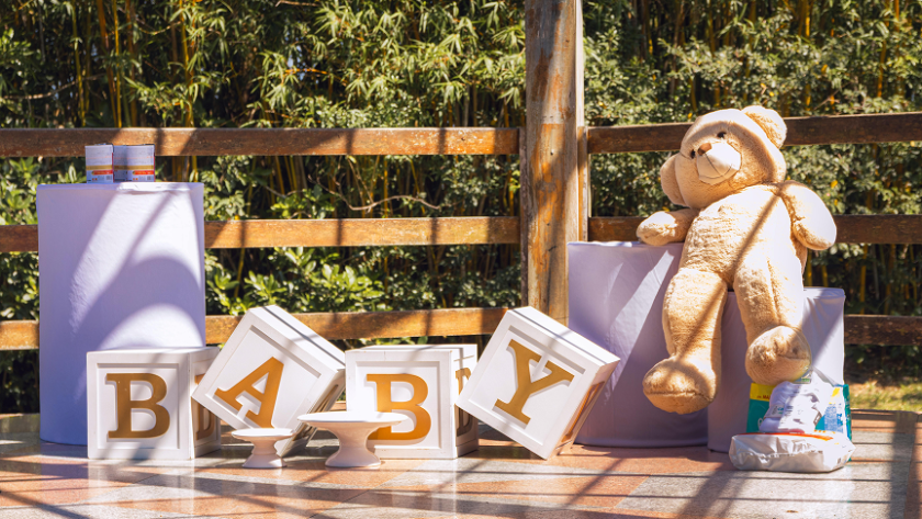 Outdoor baby shower setup featuring decorative BABY blocks, teddy bear, and gift table in a rustic garden setting.