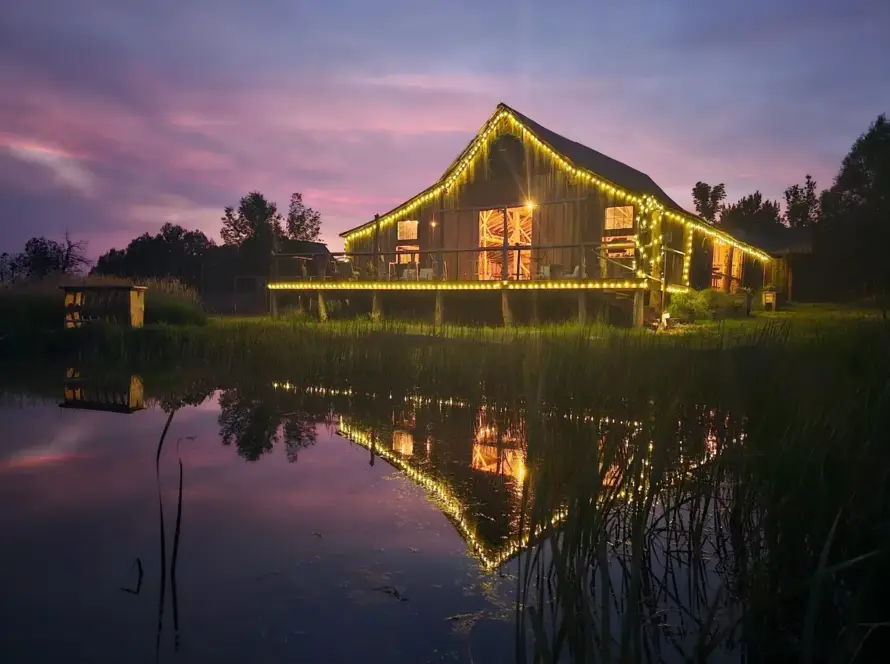 Rustic barn at Three Willows Ranch glowing with evening lights reflected on the water in Colorado