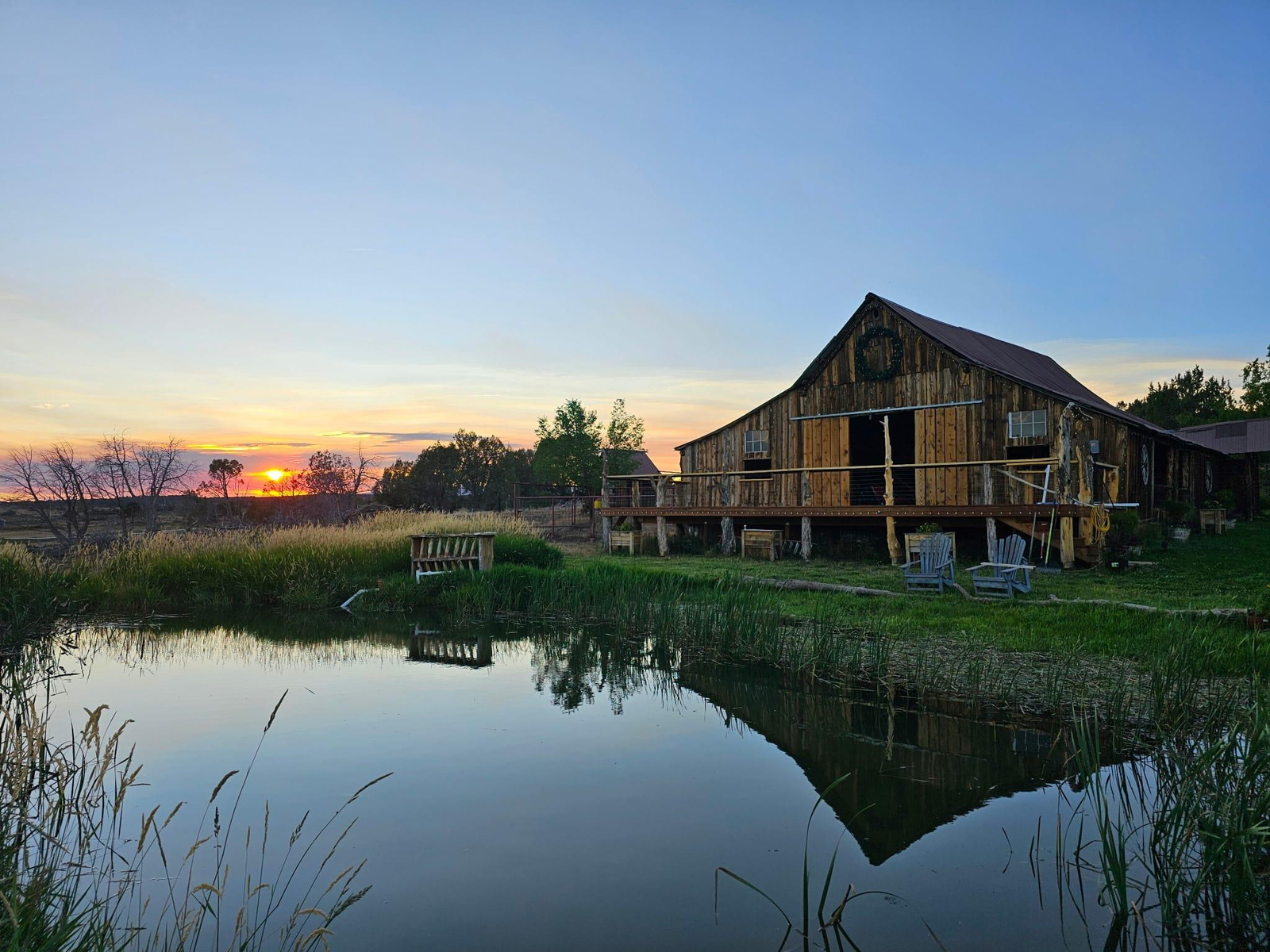 Wooden ranch barn at sunset reflecting over peaceful pond with countryside landscape view.