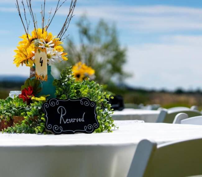 Rustic wedding table centerpiece with sunflowers, greenery, and reserved sign at outdoor ranch reception.
