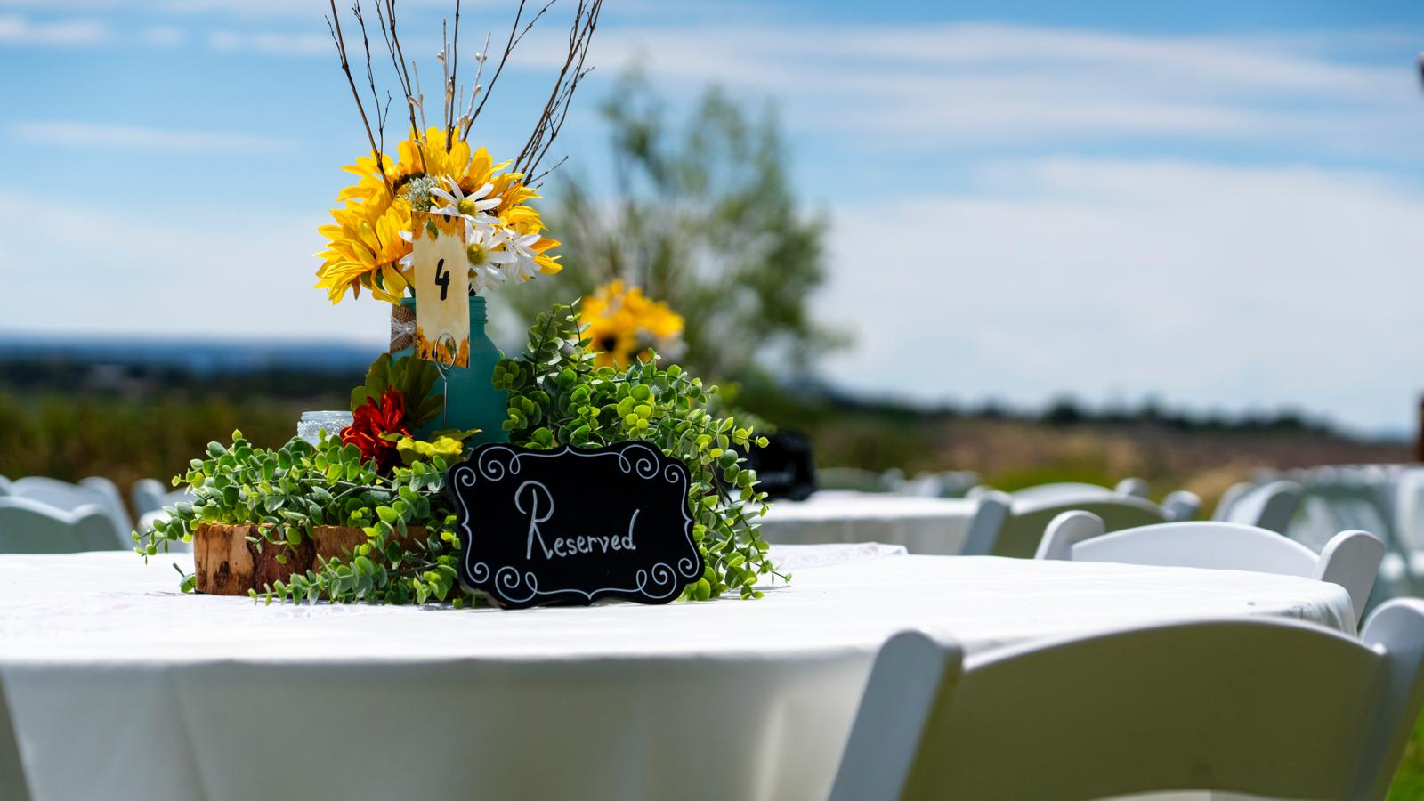 Rustic wedding table centerpiece with sunflowers, greenery, and reserved sign at outdoor ranch reception.