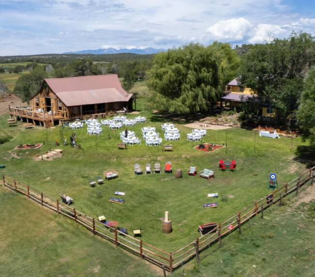 Aerial view of Three Willows Ranch rustic barn with outdoor event lawn, seating area, and mountain views in Bayfield Colorado