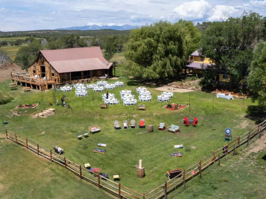 Aerial view of Three Willows Ranch rustic barn with outdoor event lawn, seating area, and mountain views in Bayfield Colorado