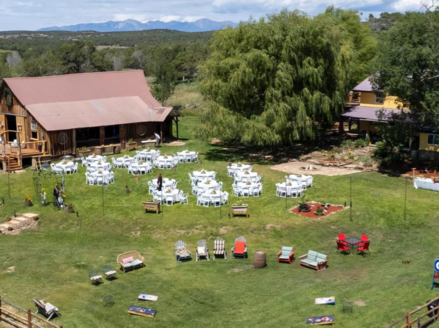 Aerial view of Three Willows Ranch rustic barn with outdoor event lawn, seating area, and mountain views in Bayfield Colorado