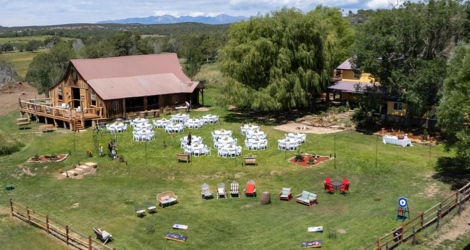 Aerial view of Three Willows Ranch rustic barn with outdoor event lawn, seating area, and mountain views in Bayfield Colorado