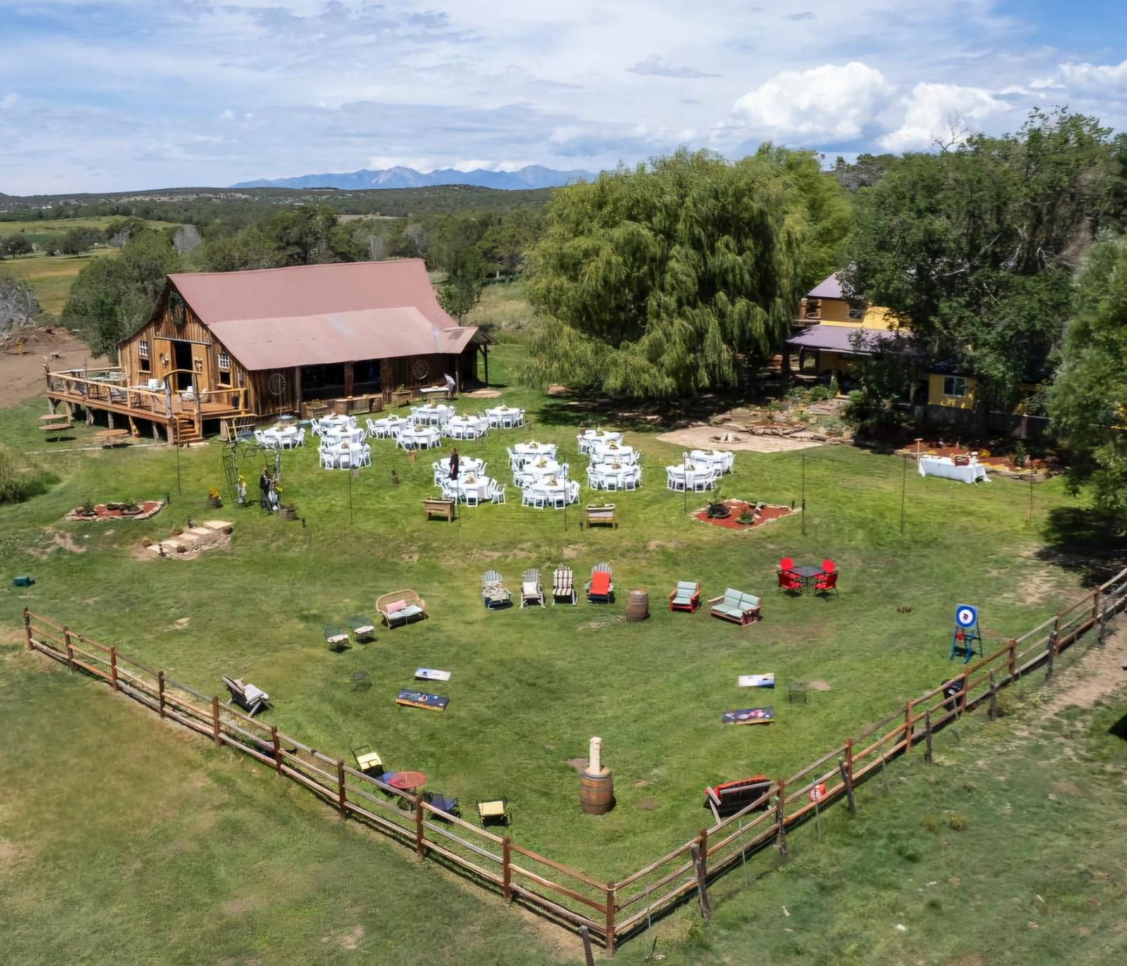 Aerial view of Three Willows Ranch rustic barn with outdoor event lawn, seating area, and mountain views in Bayfield Colorado