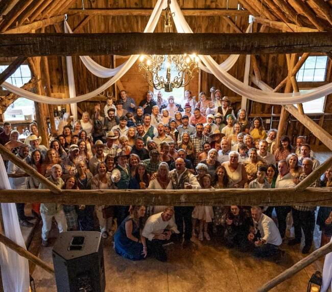 Wedding guests gathered inside a historic wooden barn reception space with chandelier and draped fabric at a rustic Colorado ranch venue.