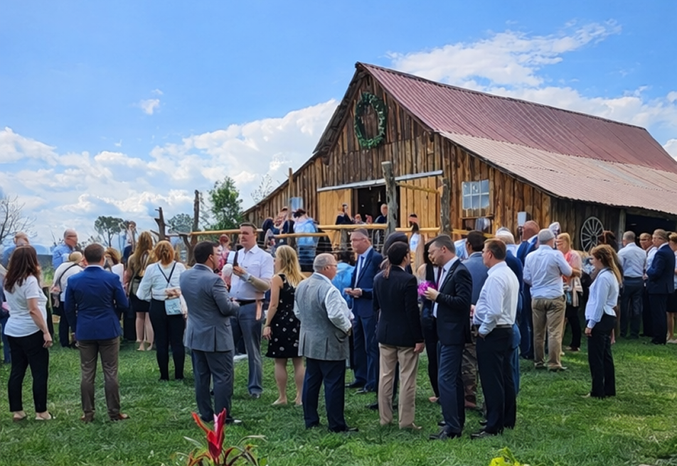 Business professionals networking at an outdoor corporate event near a rustic wooden barn in a scenic ranch setting.
