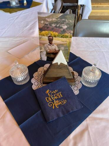 Memorial table display with framed photo, decorative items, and elegant napkin setup at a rustic event gathering.