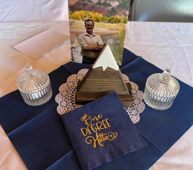 Memorial table display with framed photo, decorative items, and elegant napkin setup at a rustic event gathering.