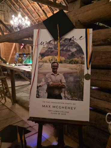 Graduation welcome sign display inside a rustic barn at a Bayfield Colorado ranch venue, decorated with cap and medal for a celebration.