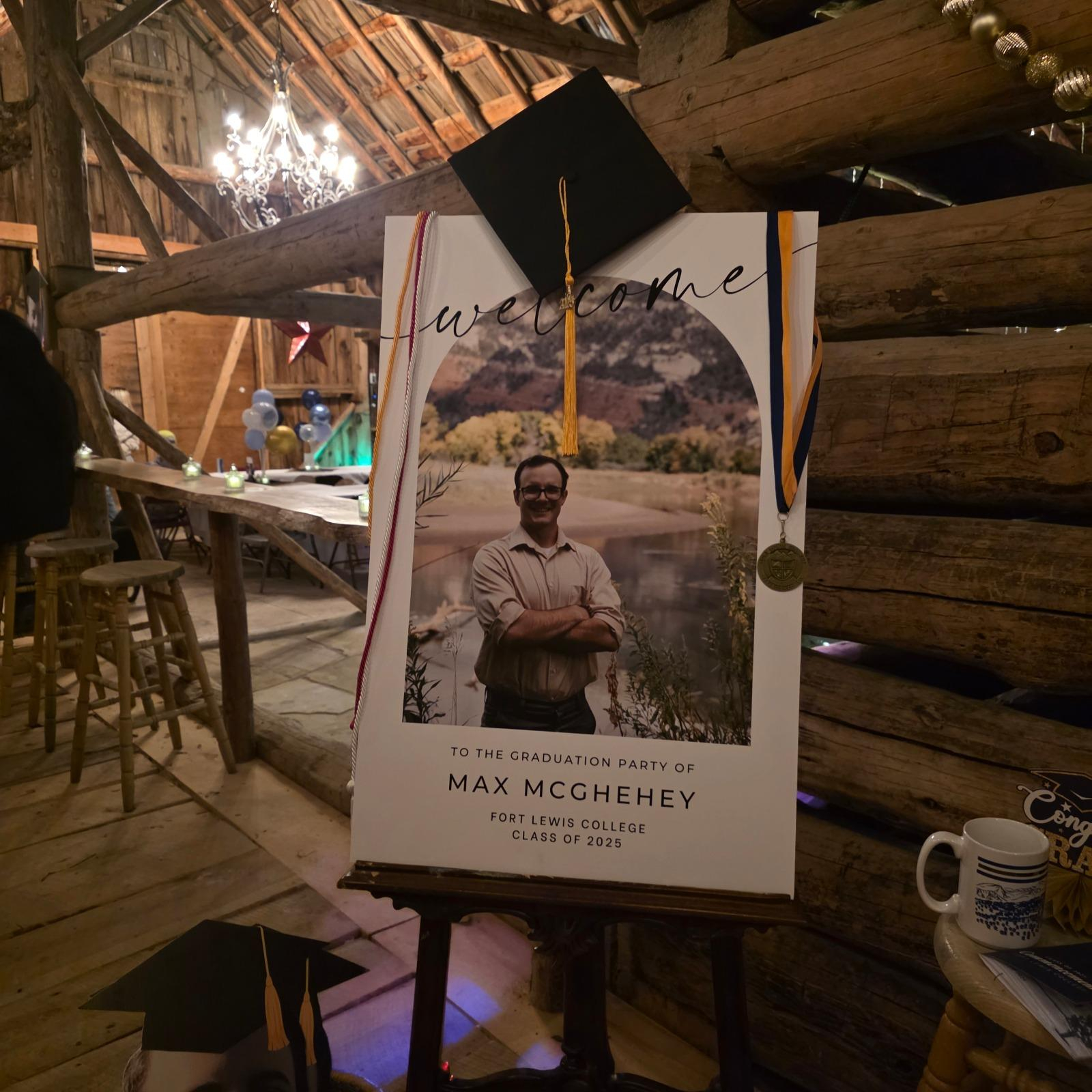 Graduation welcome sign display inside a rustic barn at a Bayfield Colorado ranch venue, decorated with cap and medal for a celebration.