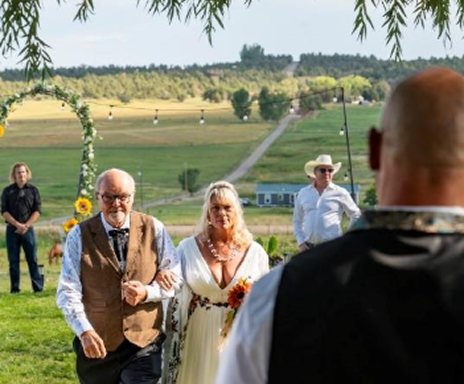 Outdoor ceremony at Three Willows Ranch near Bayfield Colorado with bride walking down the aisle under a willow arch and scenic ranch landscape in the background.