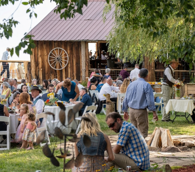 outdoor ranch reception near a historic barn with guests seated at tables, creating a lively and welcoming Colorado gathering atmosphere.