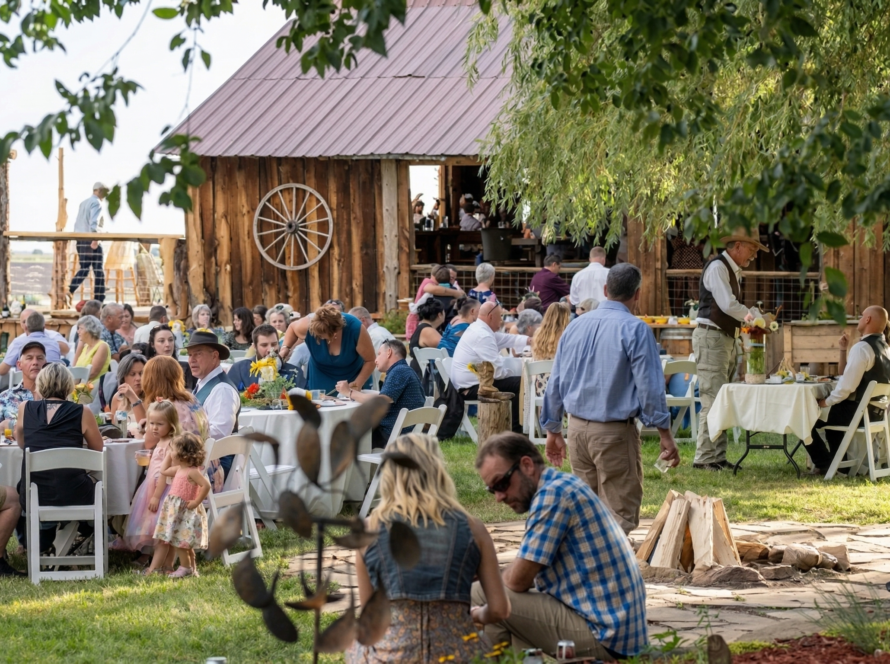 outdoor ranch reception near a historic barn with guests seated at tables, creating a lively and welcoming Colorado gathering atmosphere.
