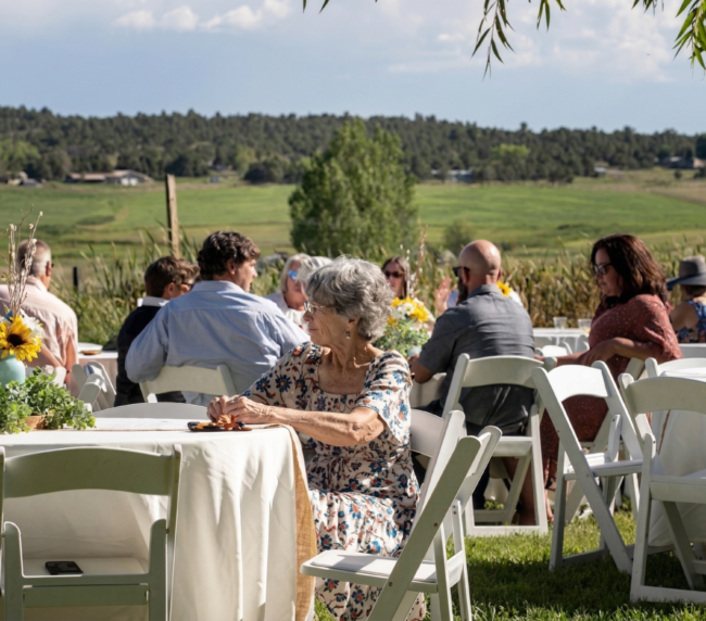 Guests seated at an outdoor ranch reception with scenic mountain and countryside views in Colorado, enjoying a relaxed and elegant gathering.