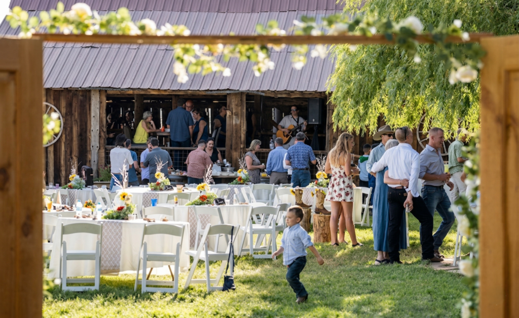 Guests mingling at an outdoor reception near a rustic barn at Three Willows Ranch, with tables, greenery, and a lively countryside atmosphere.
