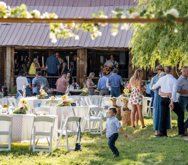 Guests mingling at an outdoor reception near a rustic barn at Three Willows Ranch, with tables, greenery, and a lively countryside atmosphere.