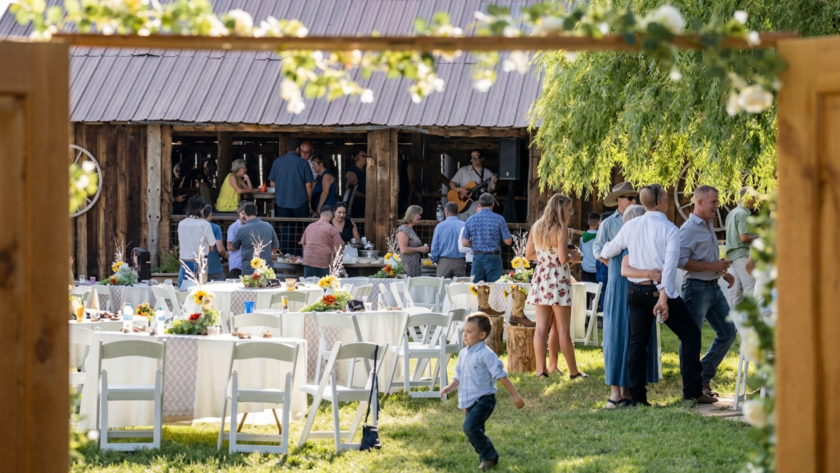 Guests mingling at an outdoor reception near a rustic barn at Three Willows Ranch, with tables, greenery, and a lively countryside atmosphere.