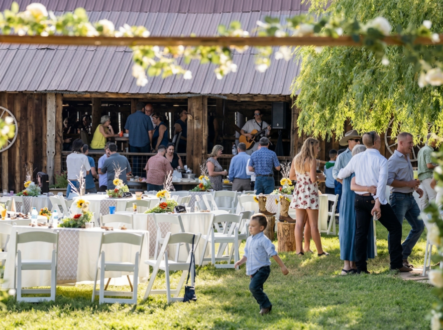 Guests mingling at an outdoor reception near a rustic barn at Three Willows Ranch, with tables, greenery, and a lively countryside atmosphere.