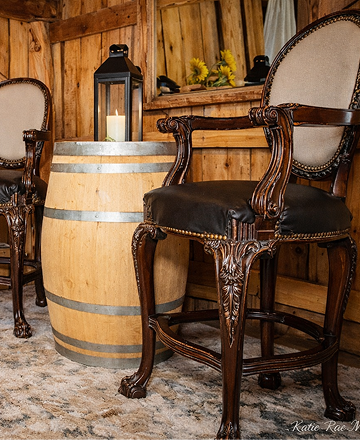 Rustic wooden barn seating area with vintage chairs, a wooden barrel table, lantern decor, and sunflower floral arrangement.