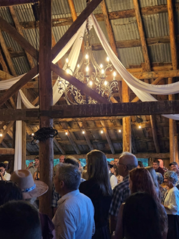 Guests gathered inside a rustic wooden barn with chandelier lighting during a wedding celebration at Three Willows Ranch.