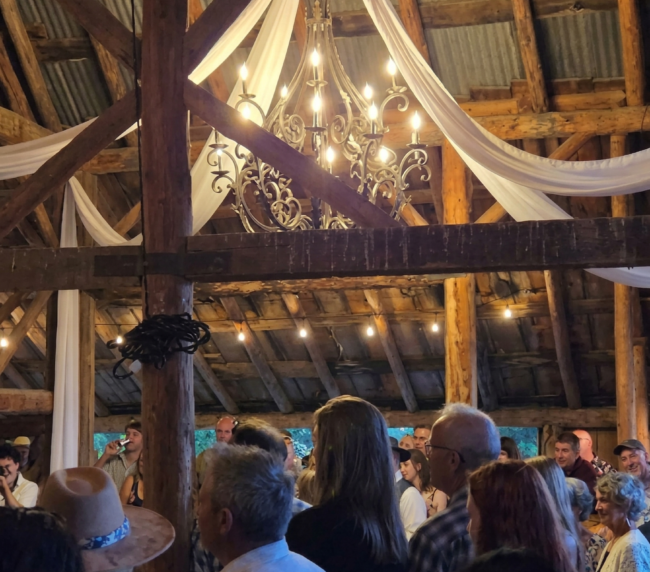 Guests gathered inside a rustic wooden barn with chandelier lighting during a wedding celebration at Three Willows Ranch.