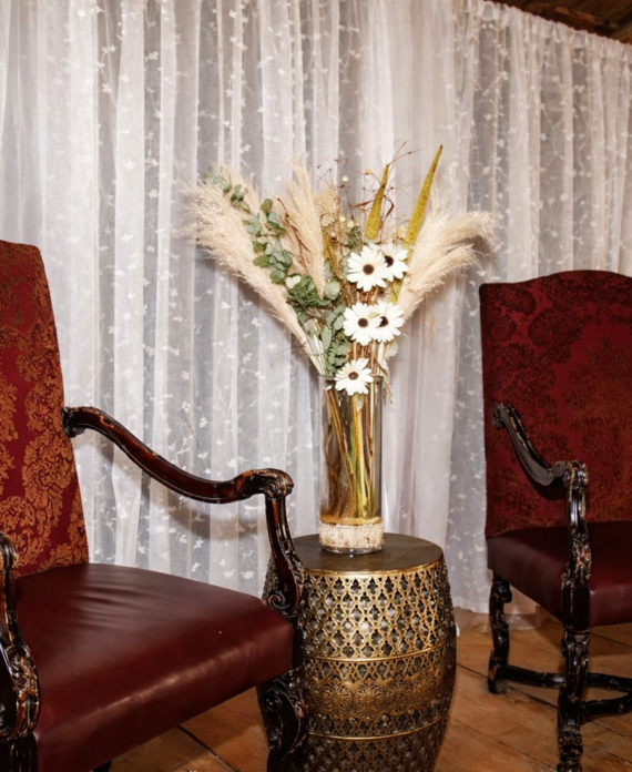 Two elegant red vintage chairs with a decorative floral arrangement between them inside a rustic barn wedding venue.