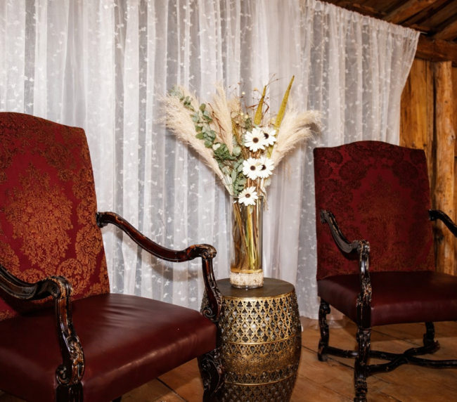 Two elegant red vintage chairs with a decorative floral arrangement between them inside a rustic barn wedding venue.