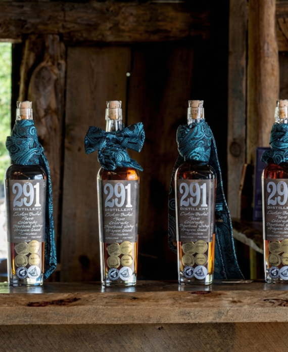 Whiskey bottles lined on a rustic wooden bar inside a historic barn, showcasing a warm and authentic ranch gathering atmosphere in Colorado.