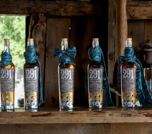 Whiskey bottles lined on a rustic wooden bar inside a historic barn, showcasing a warm and authentic ranch gathering atmosphere in Colorado.