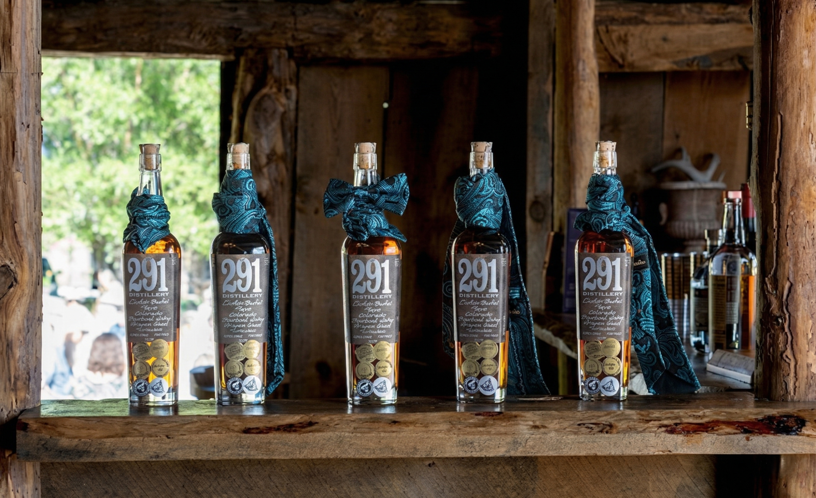 Whiskey bottles lined on a rustic wooden bar inside a historic barn, showcasing a warm and authentic ranch gathering atmosphere in Colorado.