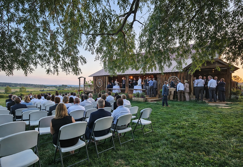 Corporate event setup with guests seated on white chairs near a rustic barn venue surrounded by scenic countryside views.