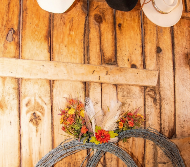 Western themed wedding decor featuring cowboy hats and floral arrangements displayed on a rustic wooden barn wall.