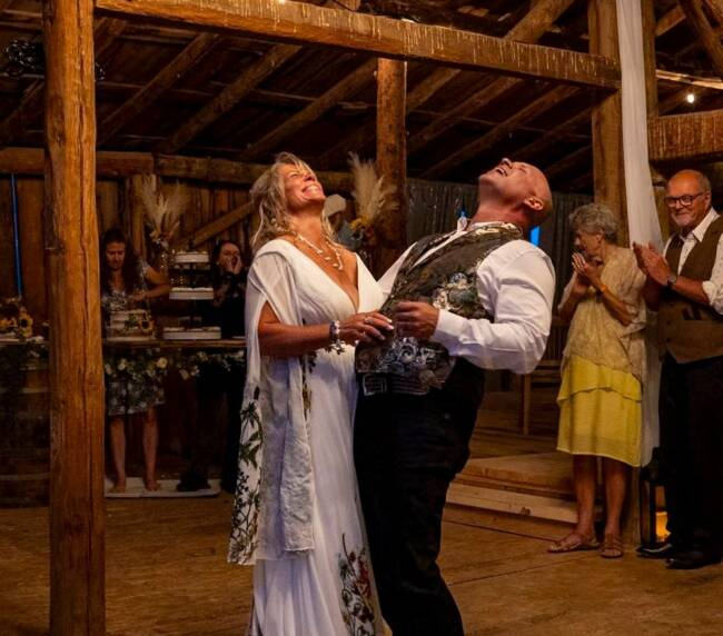 Bride and groom laughing during their first dance inside a rustic wooden barn at a Colorado ranch wedding venue.