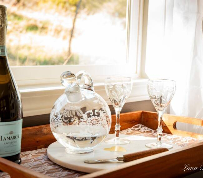 Champagne bottle with glasses on tray by sunlit window in bridal suite at rustic wedding venue