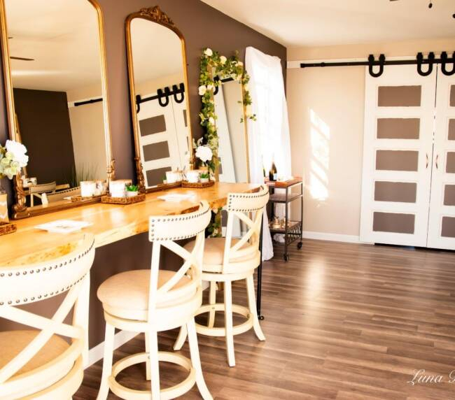 Bridal suite makeup area with wooden vanity, elegant mirrors, and chairs inside rustic barn wedding venue in Colorado
