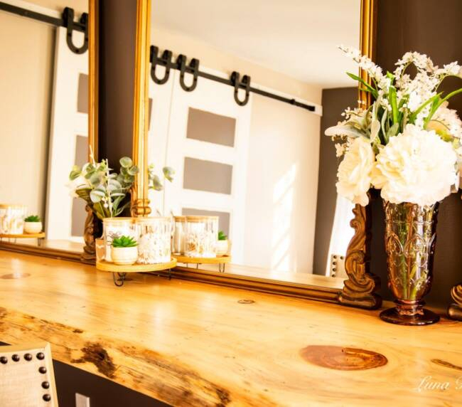 Bridal suite makeup counter with large mirrors and white floral arrangement in rustic wedding venue