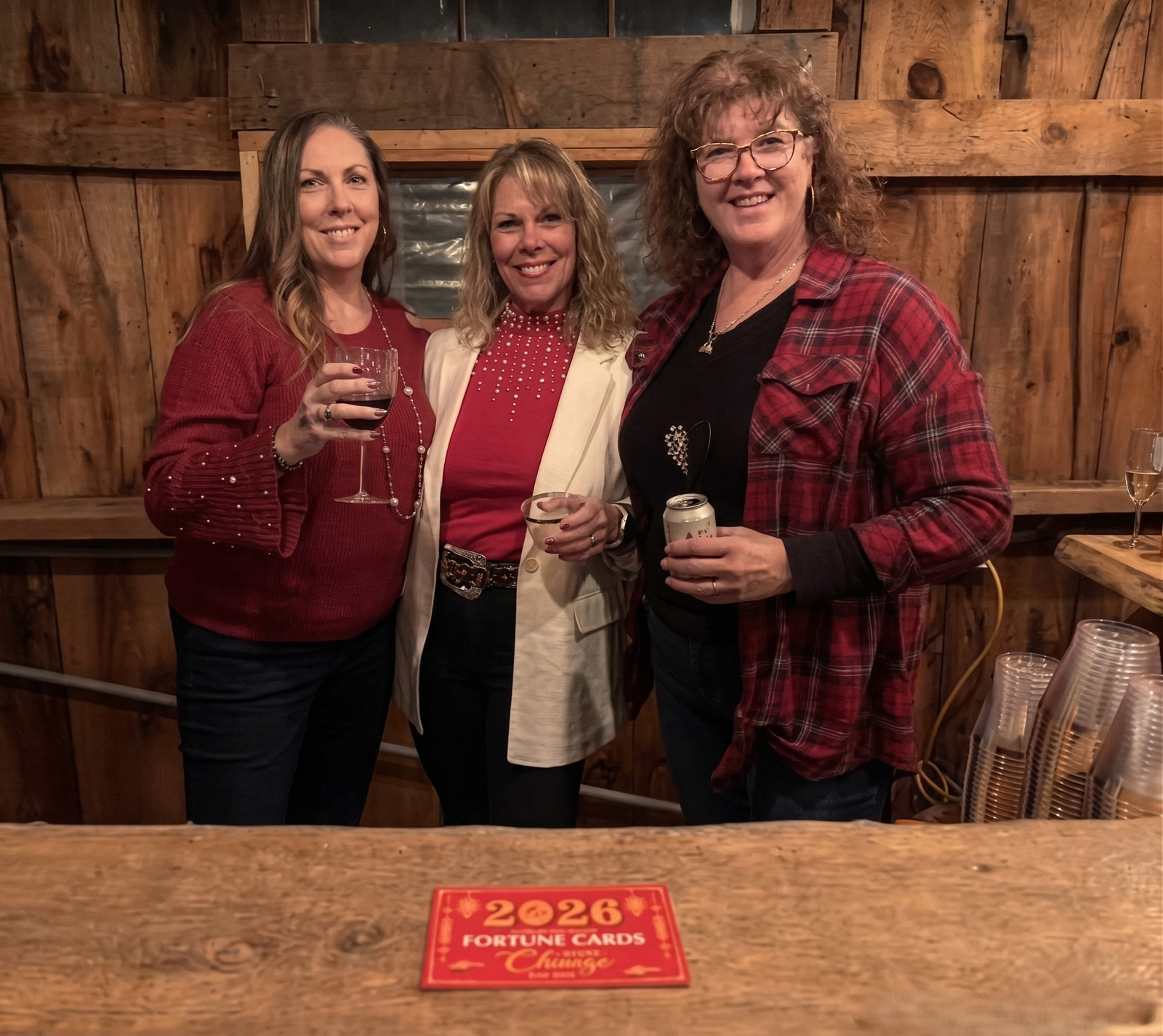 Three women smiling and holding drinks while celebrating together at a rustic barn bar during an event at Three Willows Ranch in Colorado.