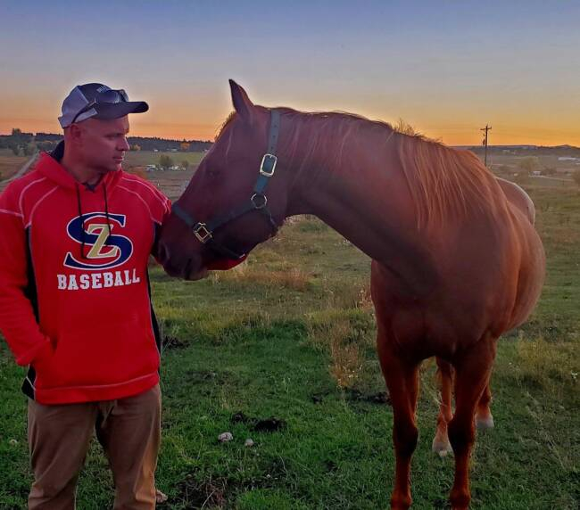 Man standing with a brown horse in an open field during sunset at a scenic Colorado ranch