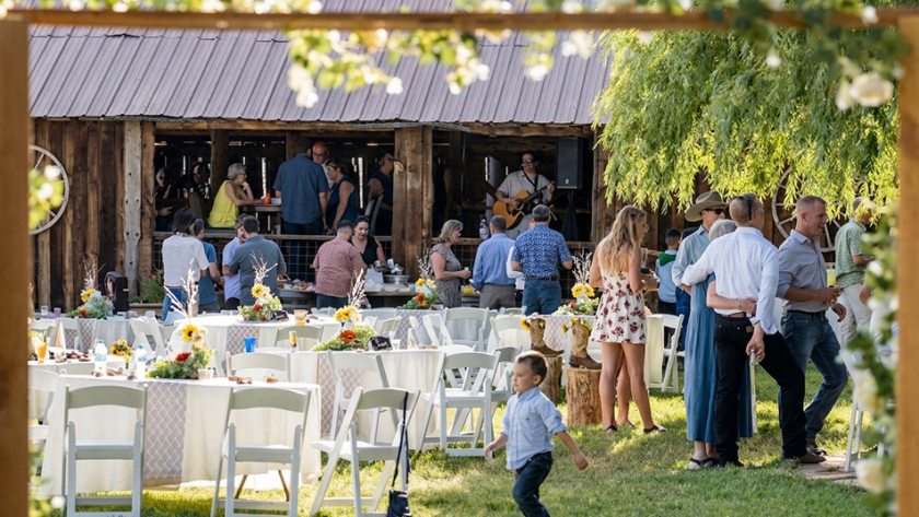 Guests mingling at an outdoor reception near a rustic barn at Three Willows Ranch, with tables, greenery, and a lively countryside atmosphere.