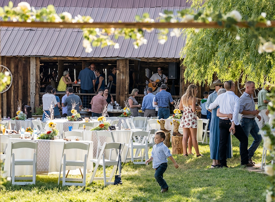 Guests mingling at an outdoor reception near a rustic barn at Three Willows Ranch, with tables, greenery, and a lively countryside atmosphere.