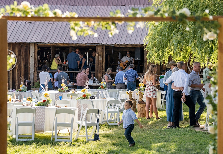 Guests mingling at an outdoor reception near a rustic barn at Three Willows Ranch, with tables, greenery, and a lively countryside atmosphere.