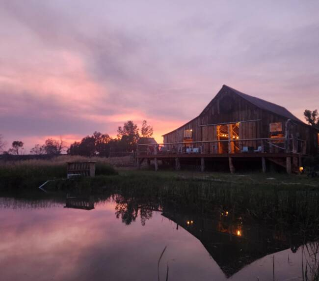 Rustic barn wedding venue at sunset with lake reflection and scenic countryside in Colorado