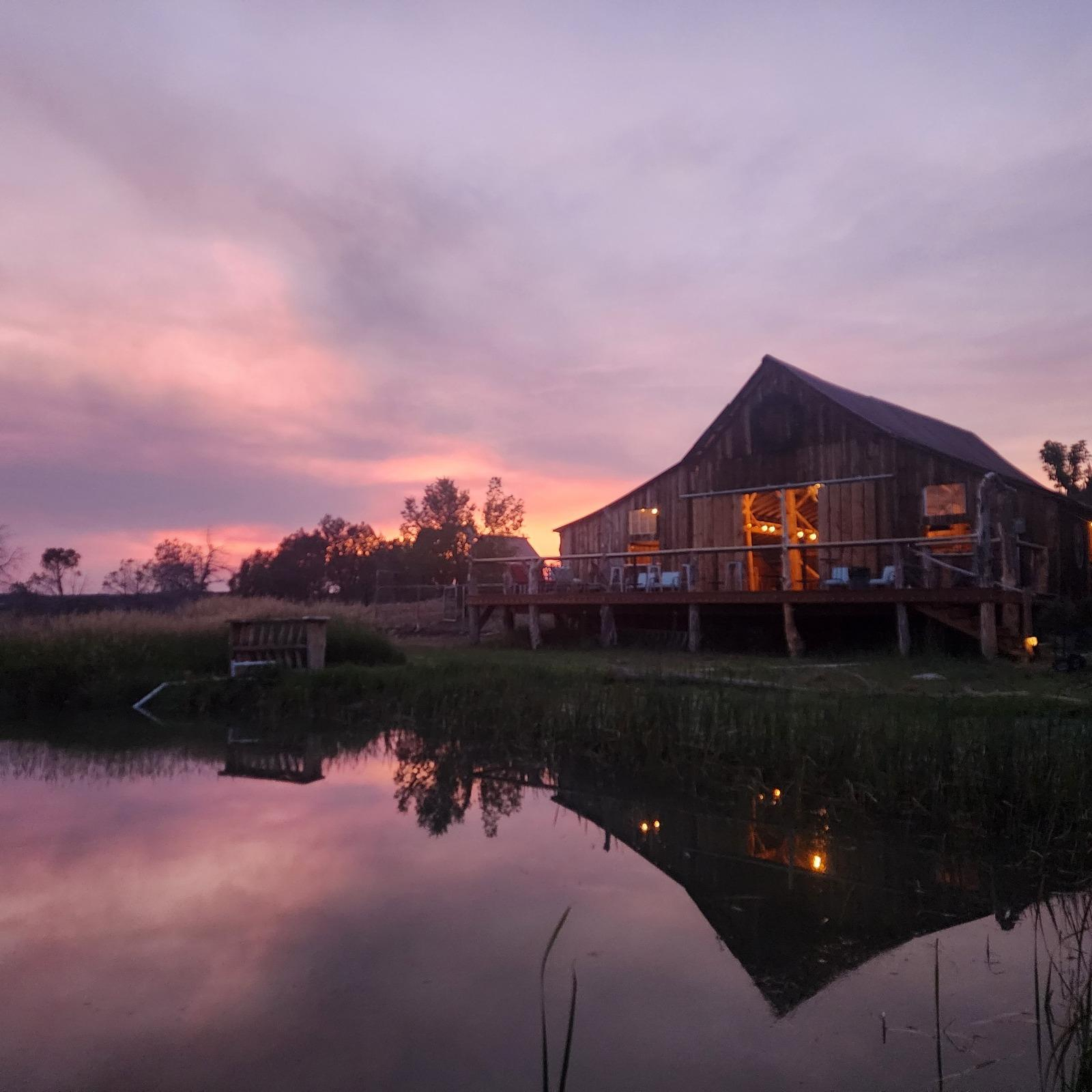 Rustic barn wedding venue at sunset with lake reflection and scenic countryside in Colorado