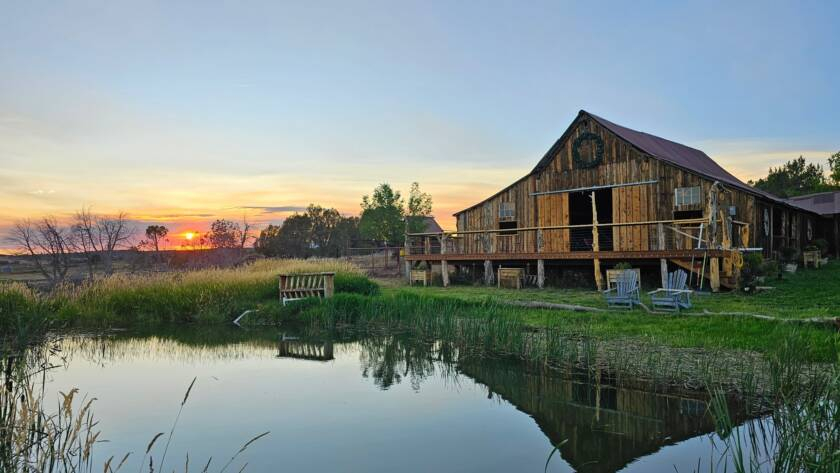 Wooden ranch barn at sunset reflecting over peaceful pond with countryside landscape view.