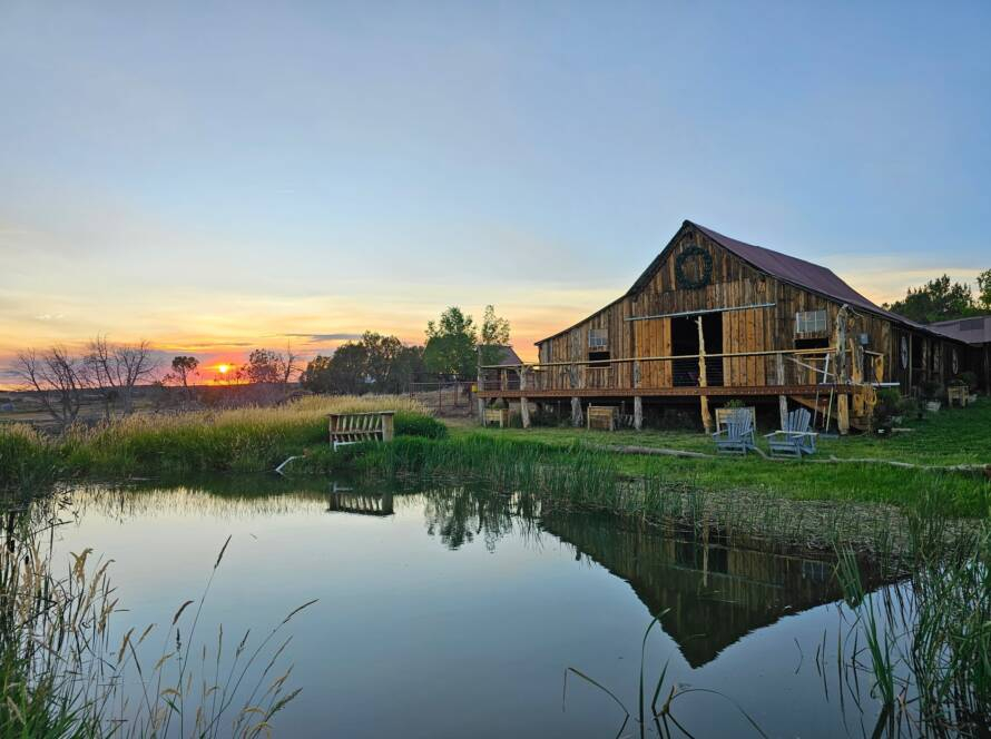 Wooden ranch barn at sunset reflecting over peaceful pond with countryside landscape view.